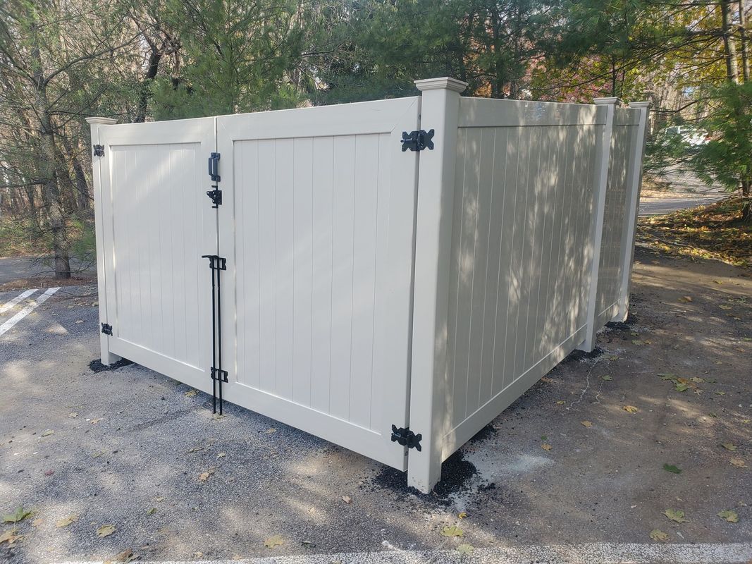 Beige fenced enclosure with black hardware on gravel. Trees in background.
