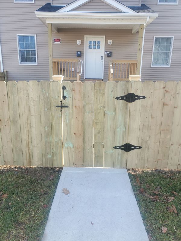 Wooden fence with a gate and a concrete walkway leading to a building's front door.