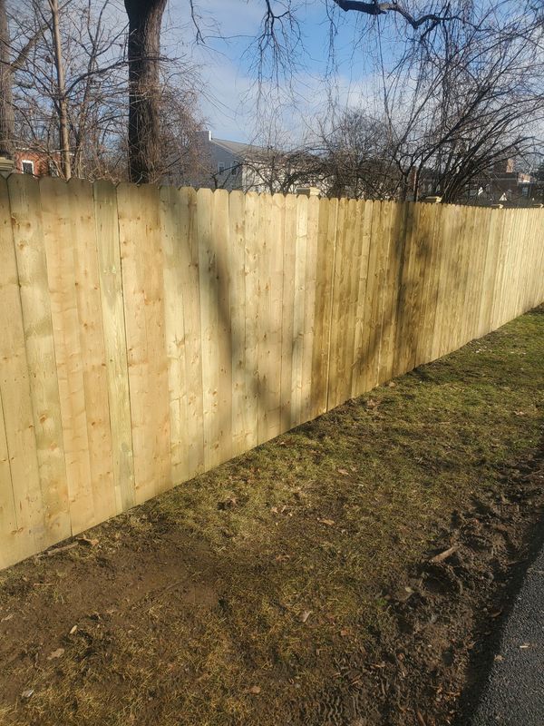 Wooden fence bordering a grassy area; trees and houses in the background on a sunny day.
