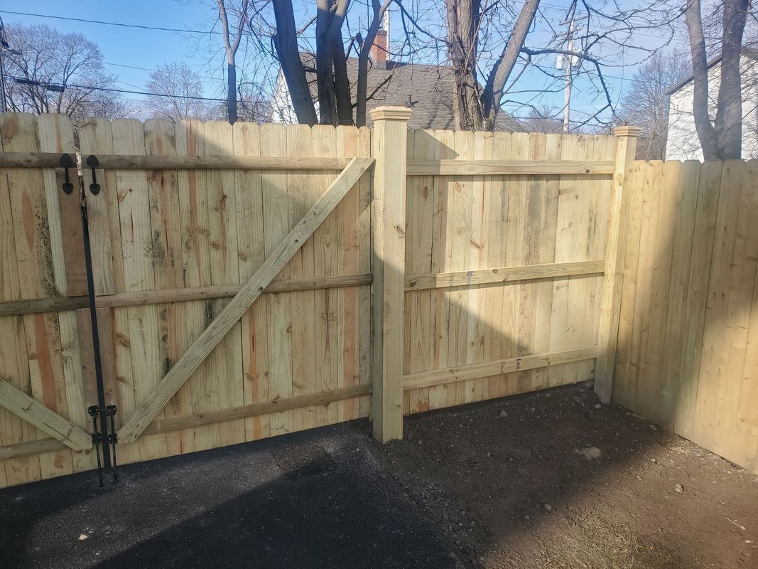 Wooden fence with gate, diagonal brace, post with decorative cap, outdoor setting.