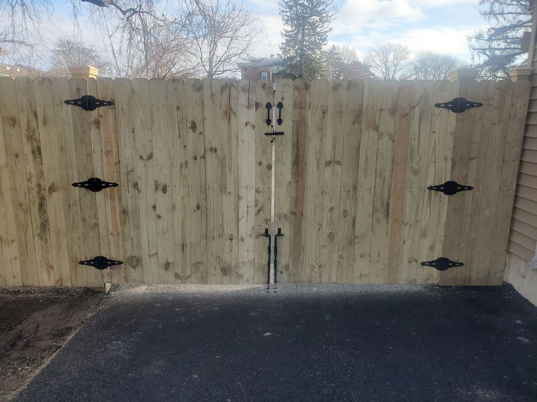 Wooden gate with decorative black hinges and latch, set on asphalt driveway.