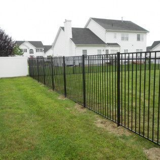 Black metal fence surrounding a grassy backyard, with white houses in the background.