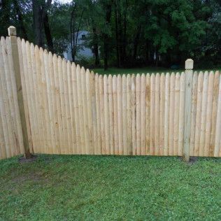 Wooden picket fence in a grassy yard with trees in the background.