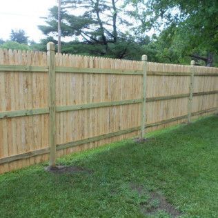 Wooden fence in a grassy backyard, with trees in the background and a cloudy sky.