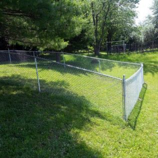 Chain-link fence on a grassy hill in a yard with trees in the background.