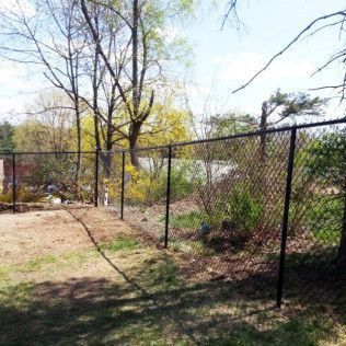 Green chain-link fence bordering a lawn with a stone wall, tree, and house.