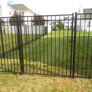 Black metal fence with gate in a grassy backyard, residential setting.