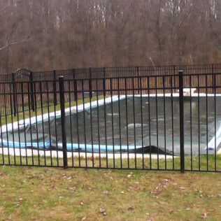 Black fenced-in pool covered with a black tarp, in front of trees.