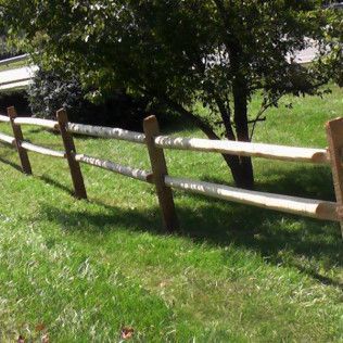 Wooden split-rail fence in a grassy yard with a tree in the background.