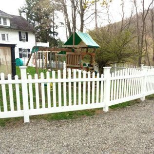 White picket fence encloses a yard with a swing set and house.