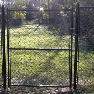 Black chain-link fence gate in a grassy yard, with green trees in the background.