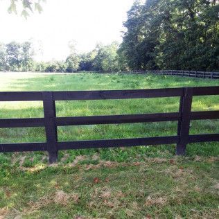 Dark brown fence in front of a grassy field, with trees in the background.
