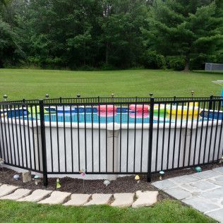Above-ground pool surrounded by black metal fence, with grass and trees in the background.
