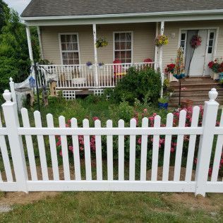 White picket fence in front of a small house with a porch and flower decorations.