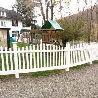 White picket fence encloses a yard with a swing set and a two-story white house.