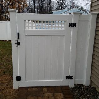 White vinyl gate with lattice top, black hardware, and vertical paneling, set in a yard.