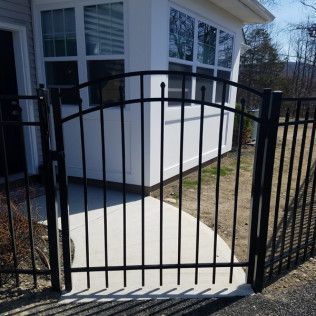 Black metal gate with arched top, leading to a white house with a sunroom.