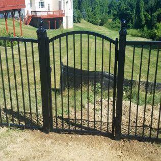 Black metal fence with matching arched gate, in front of a house and green grass.