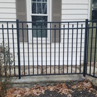 Black metal fence in front of a white house with a window and brown shutters.