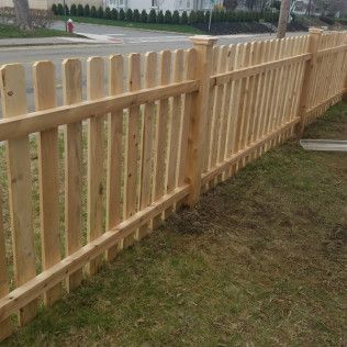 Wooden picket fence bordering a lawn, street and buildings in the background.