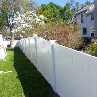 White vinyl fence along a grassy yard, with a two-story house and trees in the background.