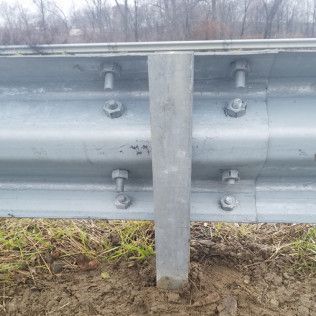 Guardrail with bolts securing metal beams to a vertical post, set in brown dirt and grass.