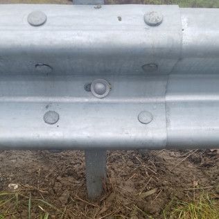 Metal guardrail with rounded rivets, installed along a muddy roadside.