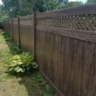 Brown wooden privacy fence with latticework, surrounded by grass and foliage.