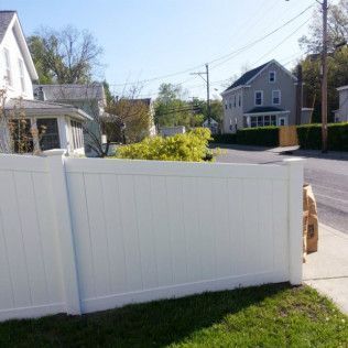 White vinyl fence in front of houses, beside a road with telephone poles. Green lawn and blue sky.