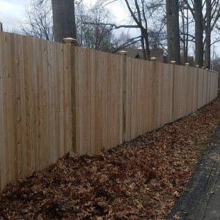 Wooden fence with post caps alongside a road with fallen leaves.