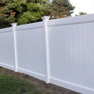 White vinyl fence with decorative posts, surrounding green grass with trees in the background.
