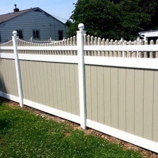 White and beige vinyl fence in front of a house and green lawn on a sunny day.
