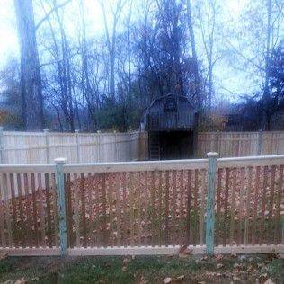 Wooden fence surrounds a yard with fallen leaves and a small barn-like structure in the distance.