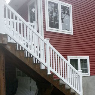 White railing and stairs leading to a red house with two windows.