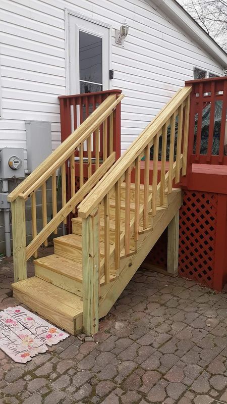 Wooden outdoor staircase leading up to a red deck, built against a white house with a door.