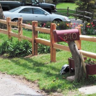 A red mailbox on a split-rail fence, address 340, with a car and truck visible in the background.