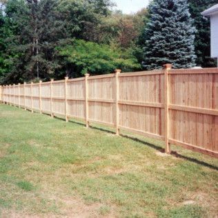 Wooden fence in a grassy backyard, separating the yard from trees and a house.
