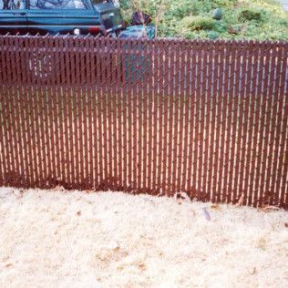 Brown chain-link fence with privacy slats, in front of a blurred-out green vehicle and foliage, in a yard.