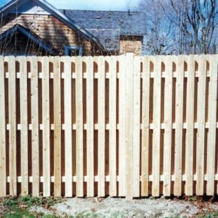 Wooden picket fence in front of a house with a gray roof and a blue sky.
