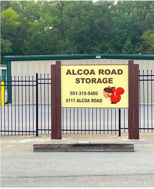 Front view of Alcoa Road Storage facility sign behind a black metal fence, displaying the business name, phone number, and address.