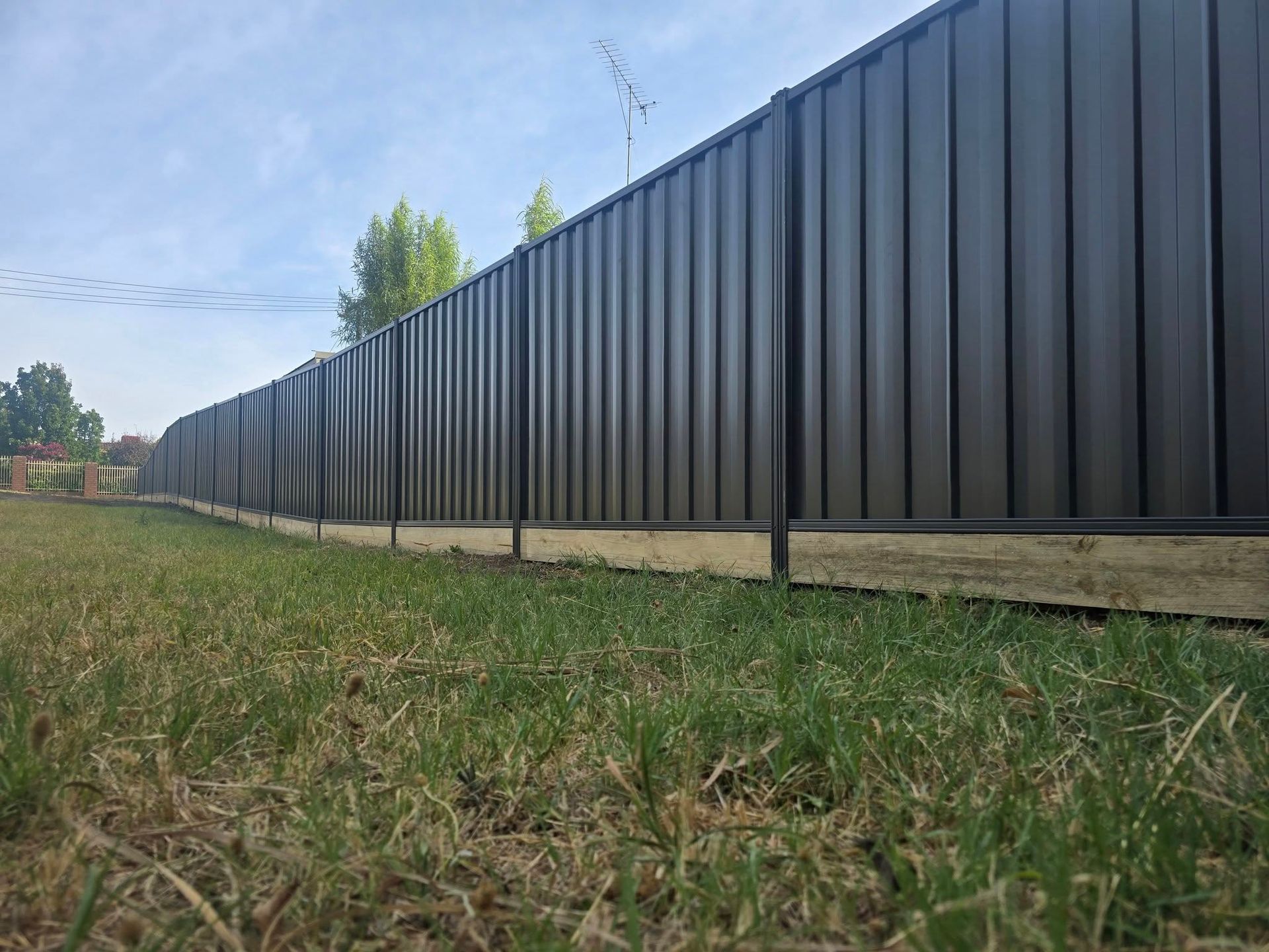 Gray vertical slat gate in a gravel area between a brick wall and wooden fence.