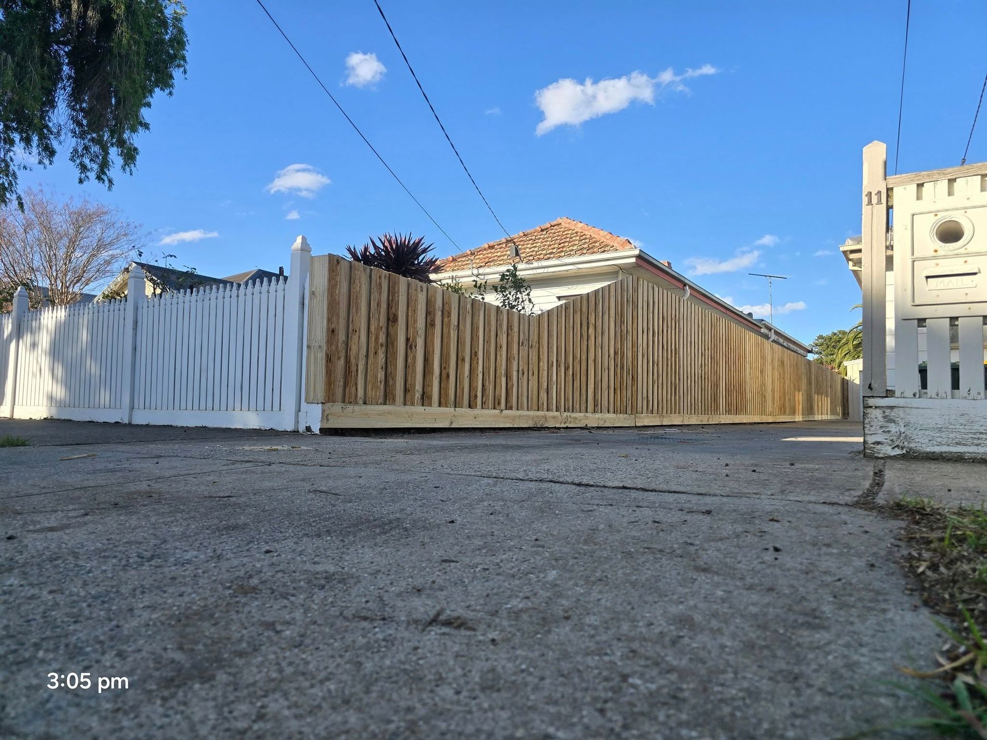 A long wooden fence, partially painted white, encloses a yard. Overhead are power lines under a blue sky.
