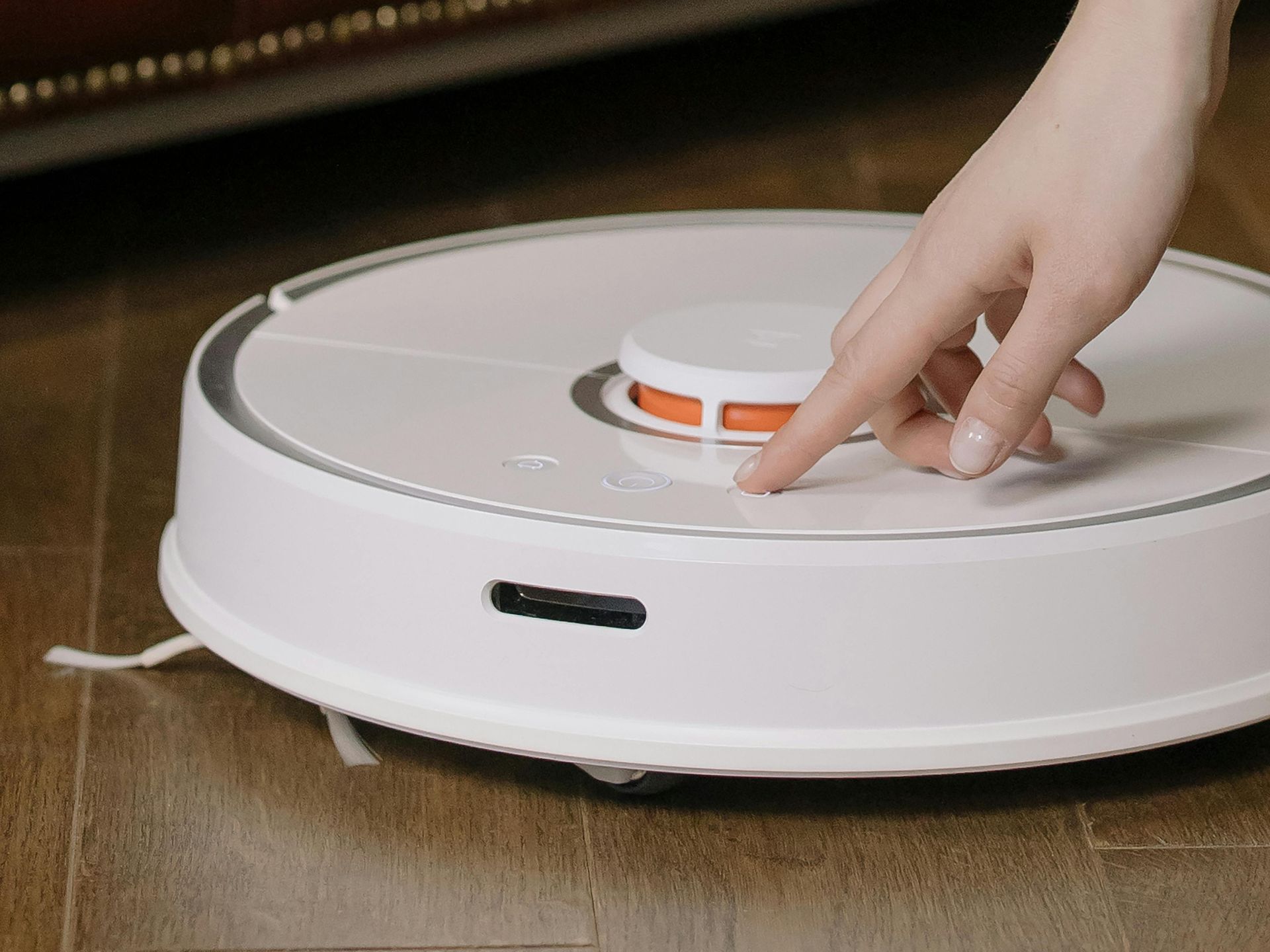 A person is pressing a button on a robot vacuum cleaner.