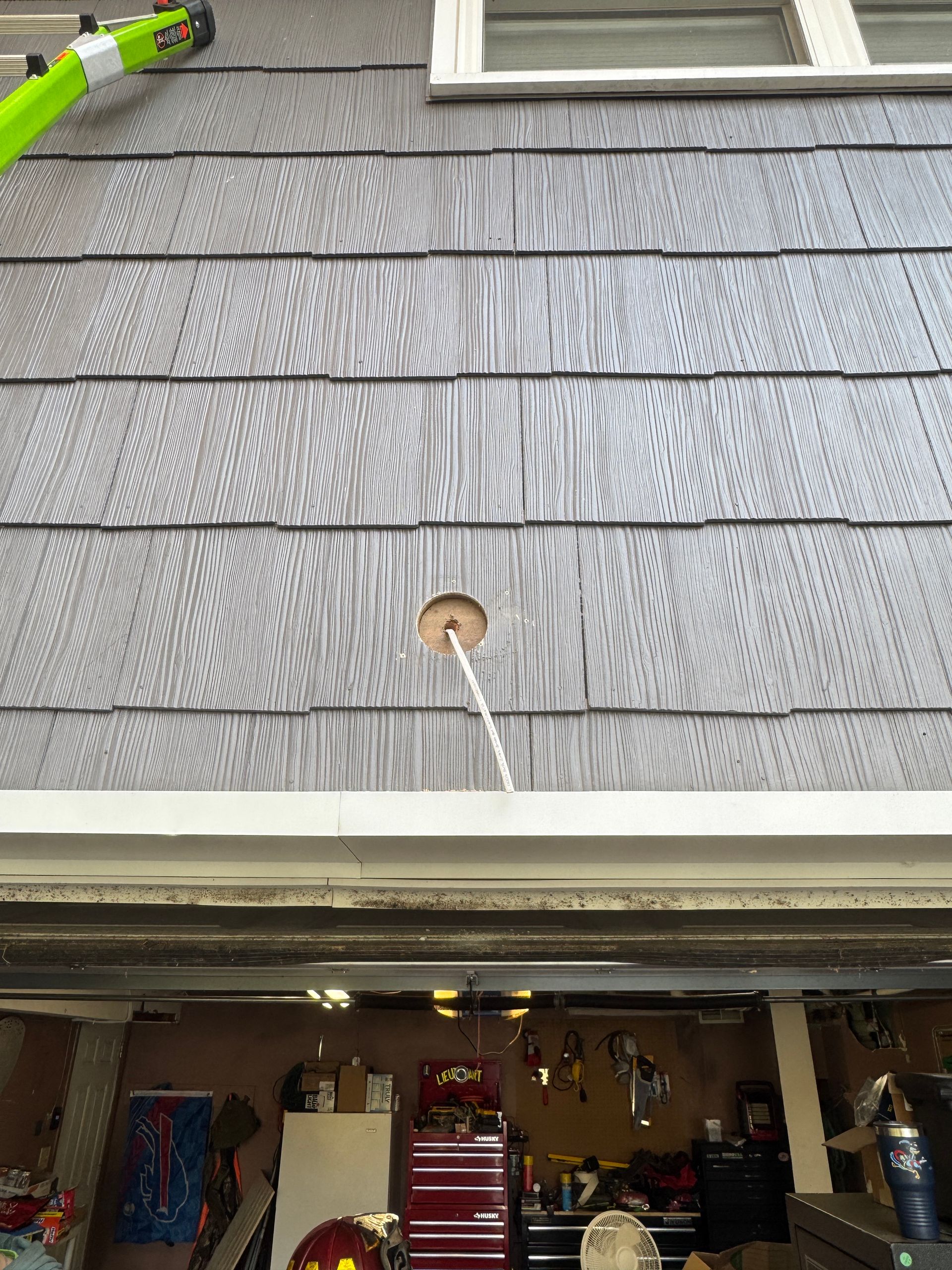 Hole drilled in gray siding, above a garage. A white cord hangs from the hole.