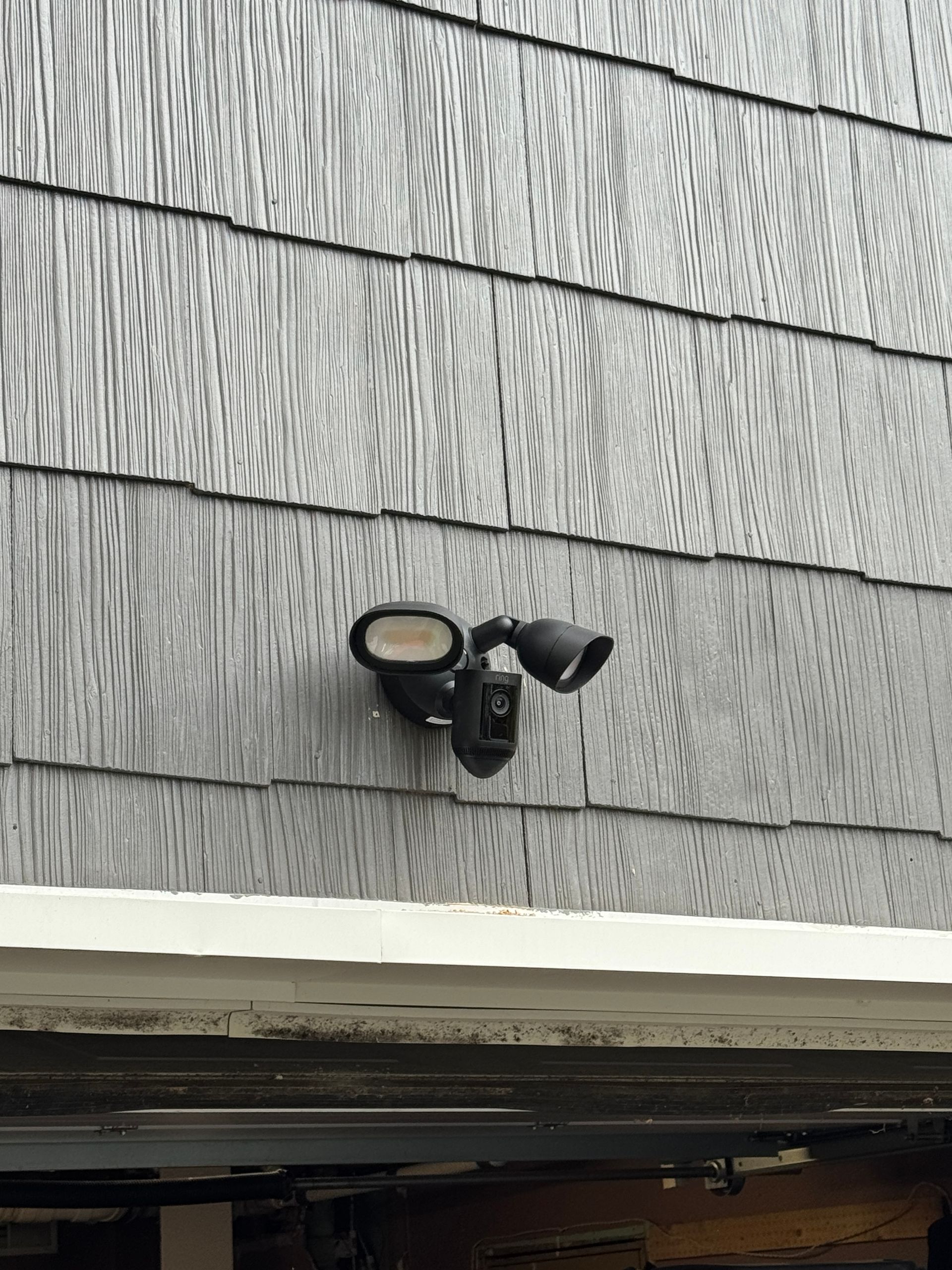 Security camera with two lights mounted on gray siding.