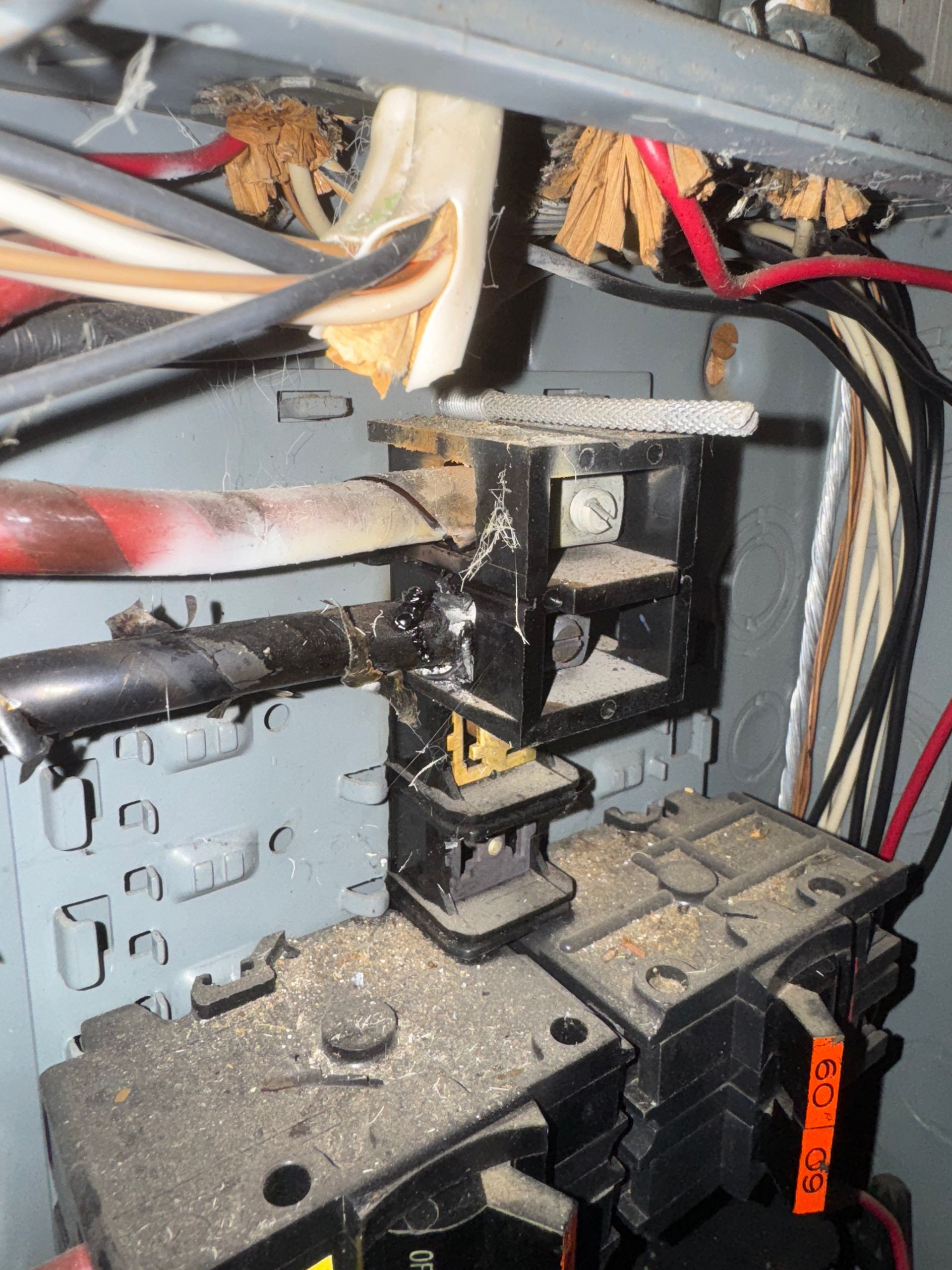 Damaged electrical panel with burnt wires and circuit breakers, inside a metal box.