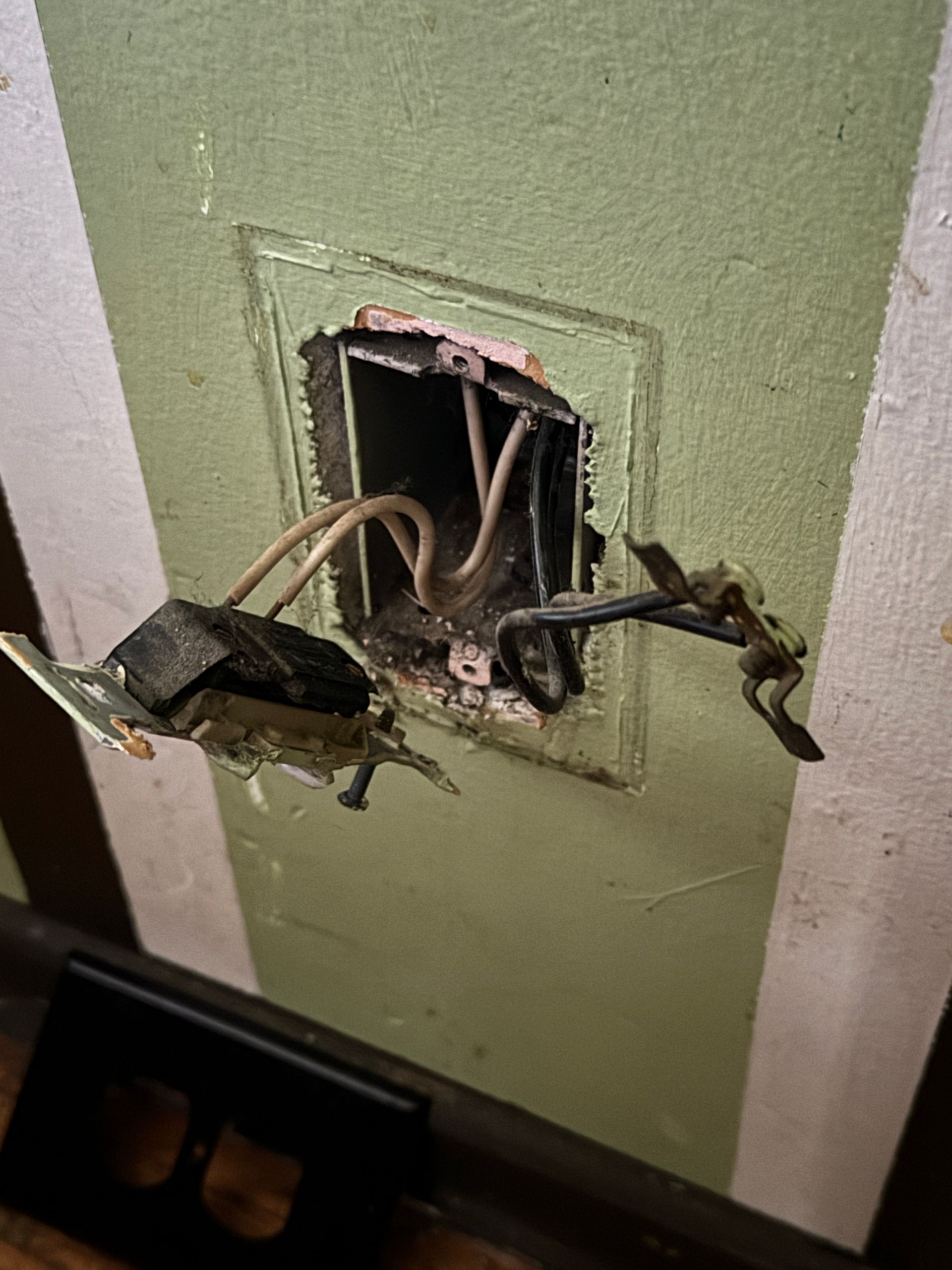 Damaged electrical outlet with exposed wires; green and white wall.