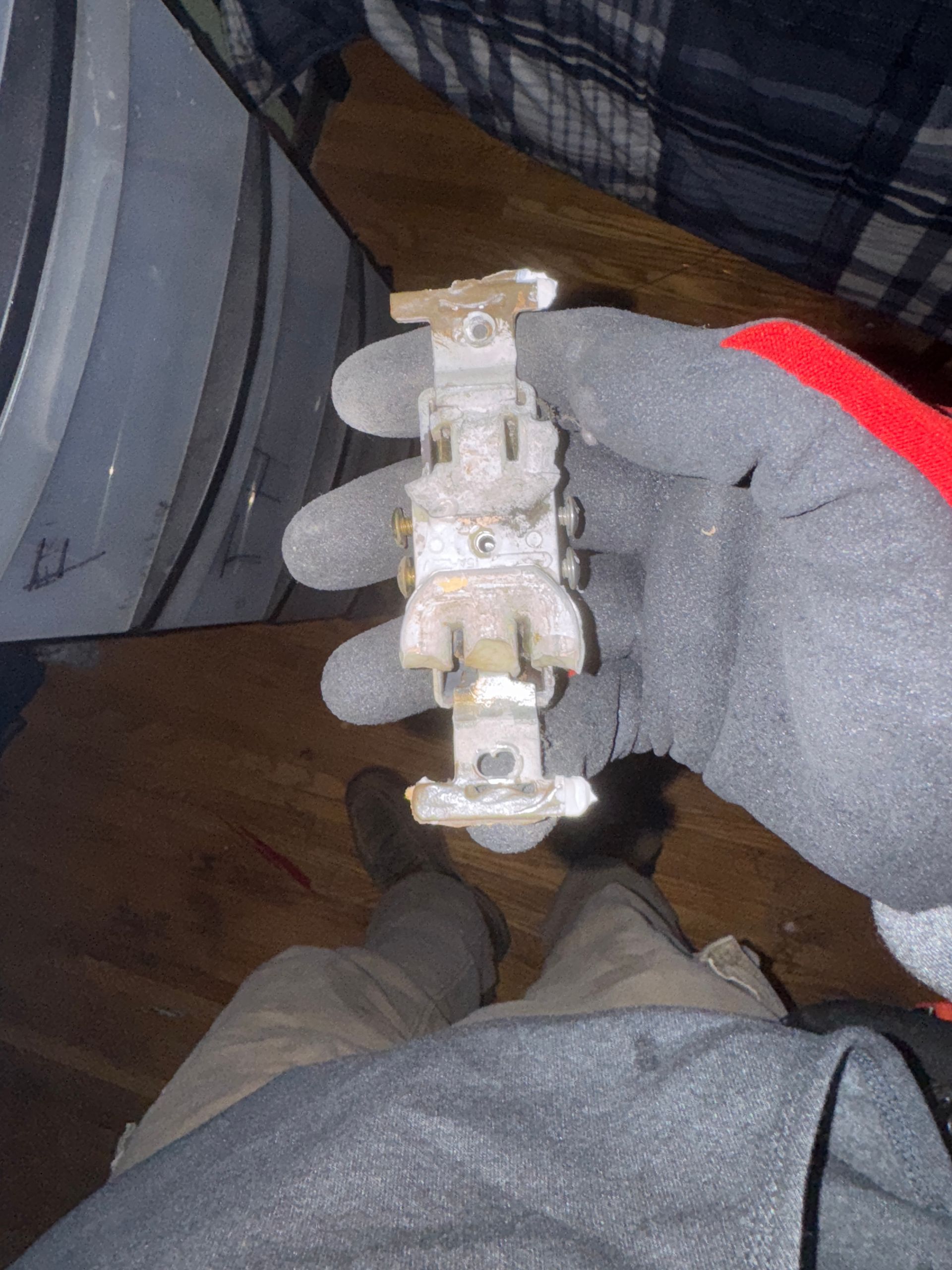 Gloved hand holding a metal, switch-like device; person seated.