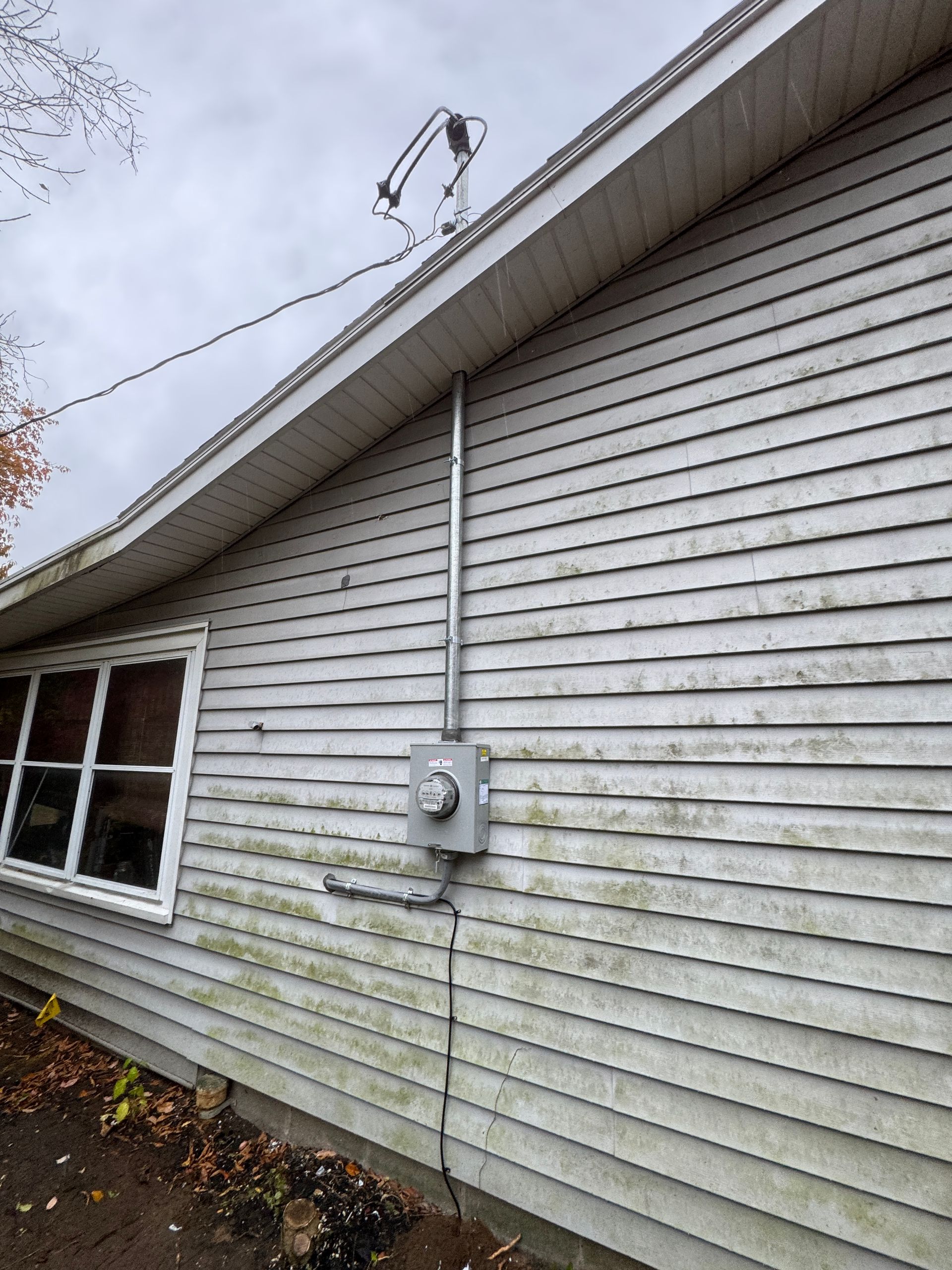 Exterior view of a weathered building with electrical conduit and a meter box. Gray siding, and a window are visible.