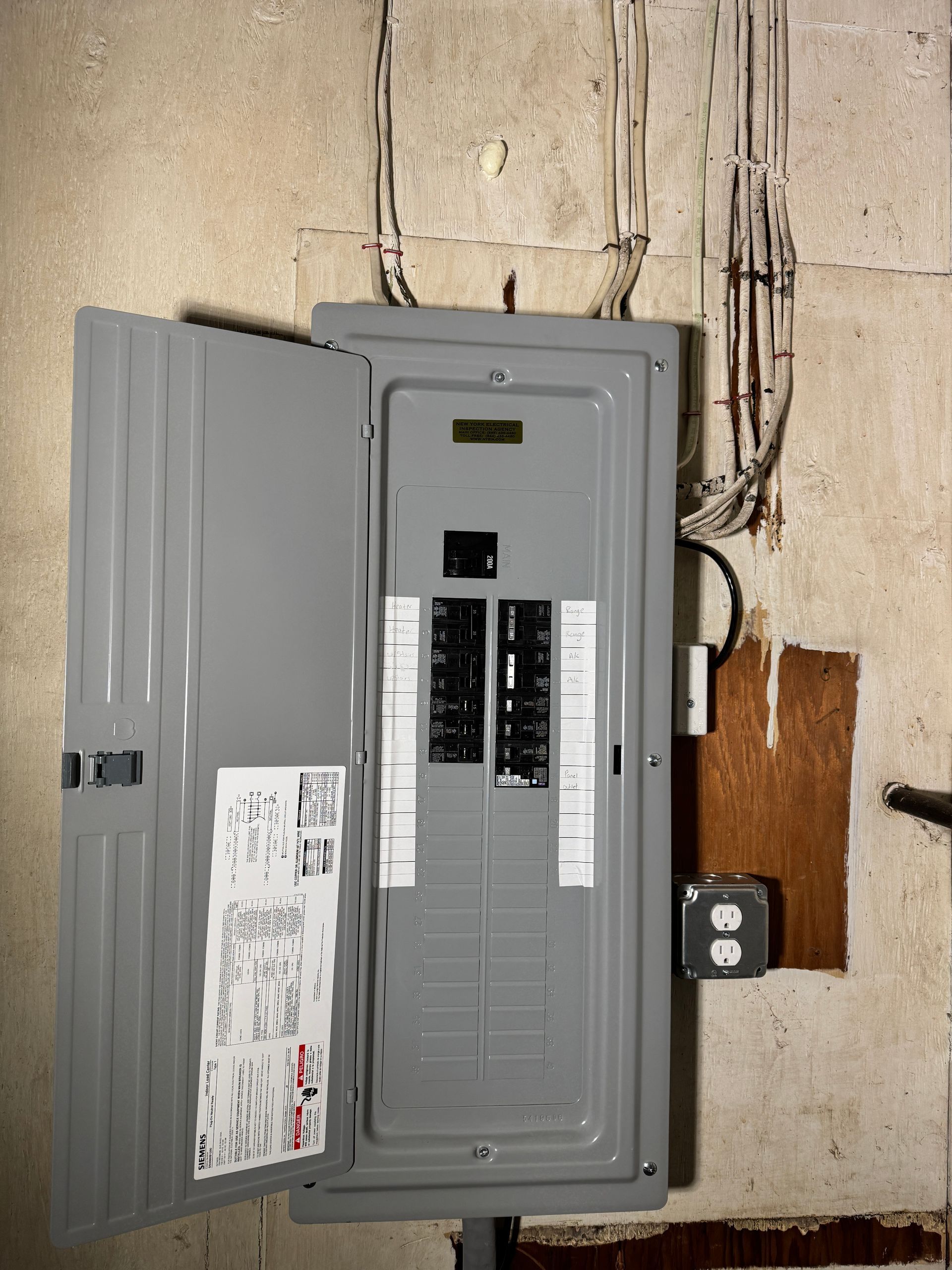 Electrical panel on a concrete wall, door open, circuit breakers visible, wires above.